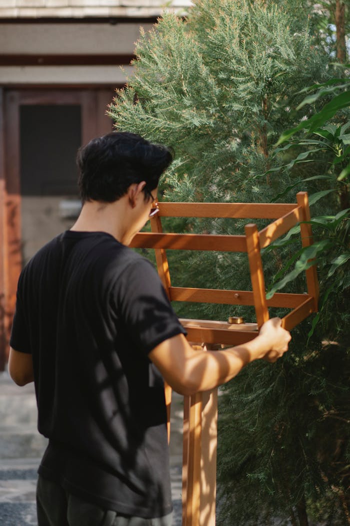 Back view of unrecognizable man in casual outfit standing in garden and installing wooden construction